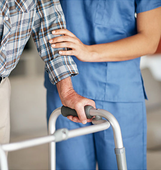 Pflegekraft stützt Patient beim gehen mit einem Rollator